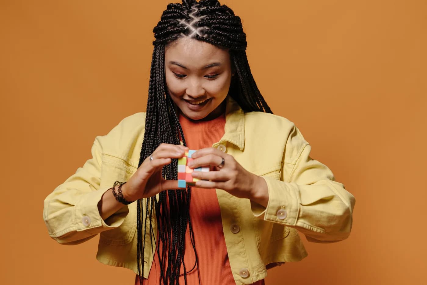 Une personne en veste jaune sourit en manipulant un casse-tête coloré, sur fond orange.